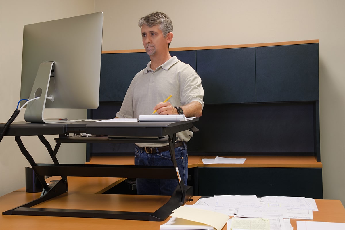 Ergonomics consultant providing a consultation to a man at a standing desk, demonstrating good workspace setup for pain management in Carlton, Melbourne.